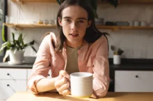 Trans muž sedí u stolu s hrnkem v ruce.