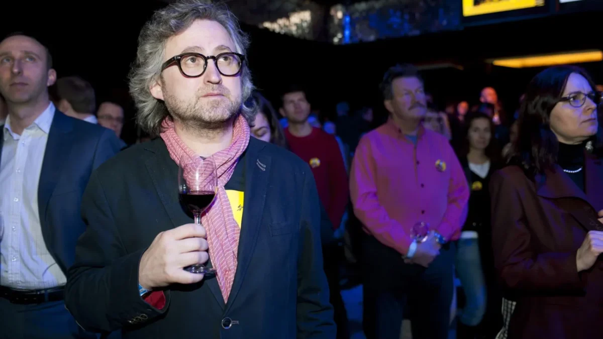 Muž stojí se sklenkou v ruce.