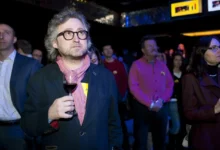 Muž stojí se sklenkou v ruce.