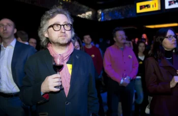 Muž stojí se sklenkou v ruce.