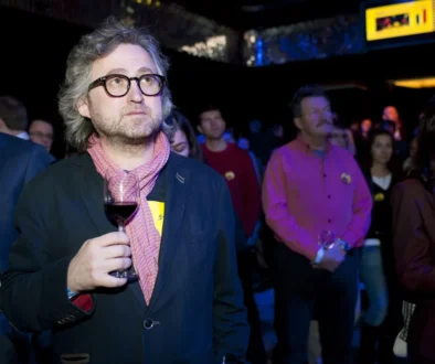 Muž stojí se sklenkou v ruce.