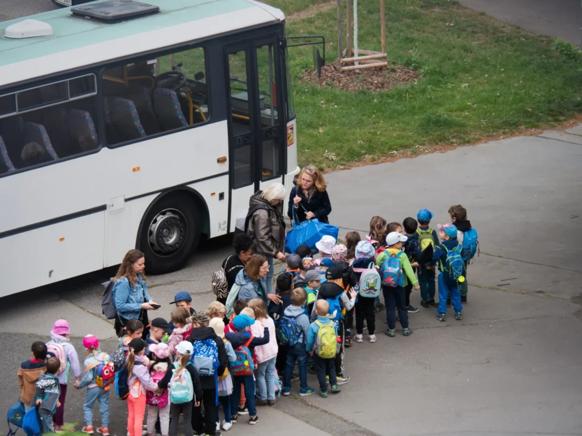 Děti stojí seřazené před autobusem.