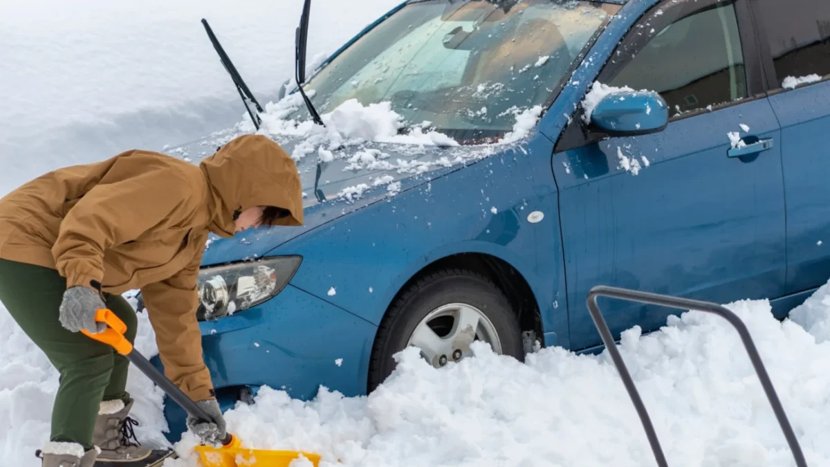 Muž odrhnující sníh u auta.