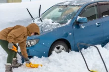 Muž odrhnující sníh u auta.