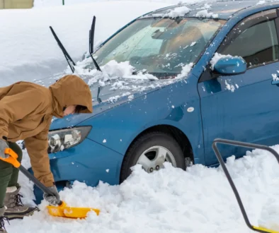 Muž odrhnující sníh u auta.