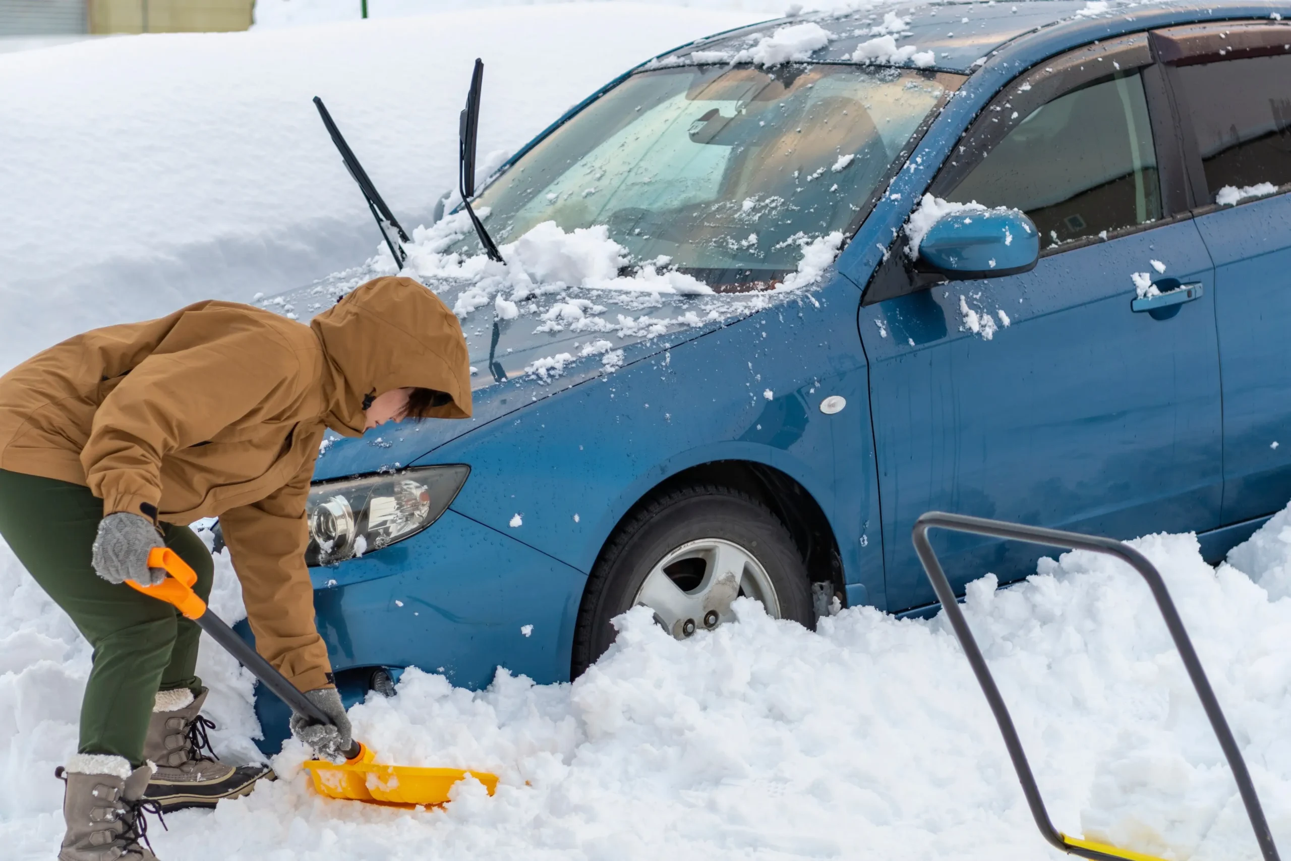 Muž odrhnující sníh u auta.