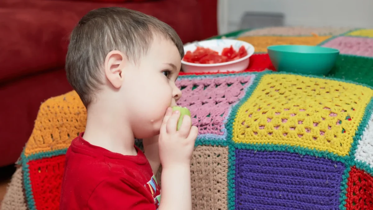 Chlapeček jí a sedí vedle gauče.