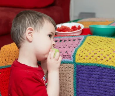 Chlapeček jí a sedí vedle gauče.