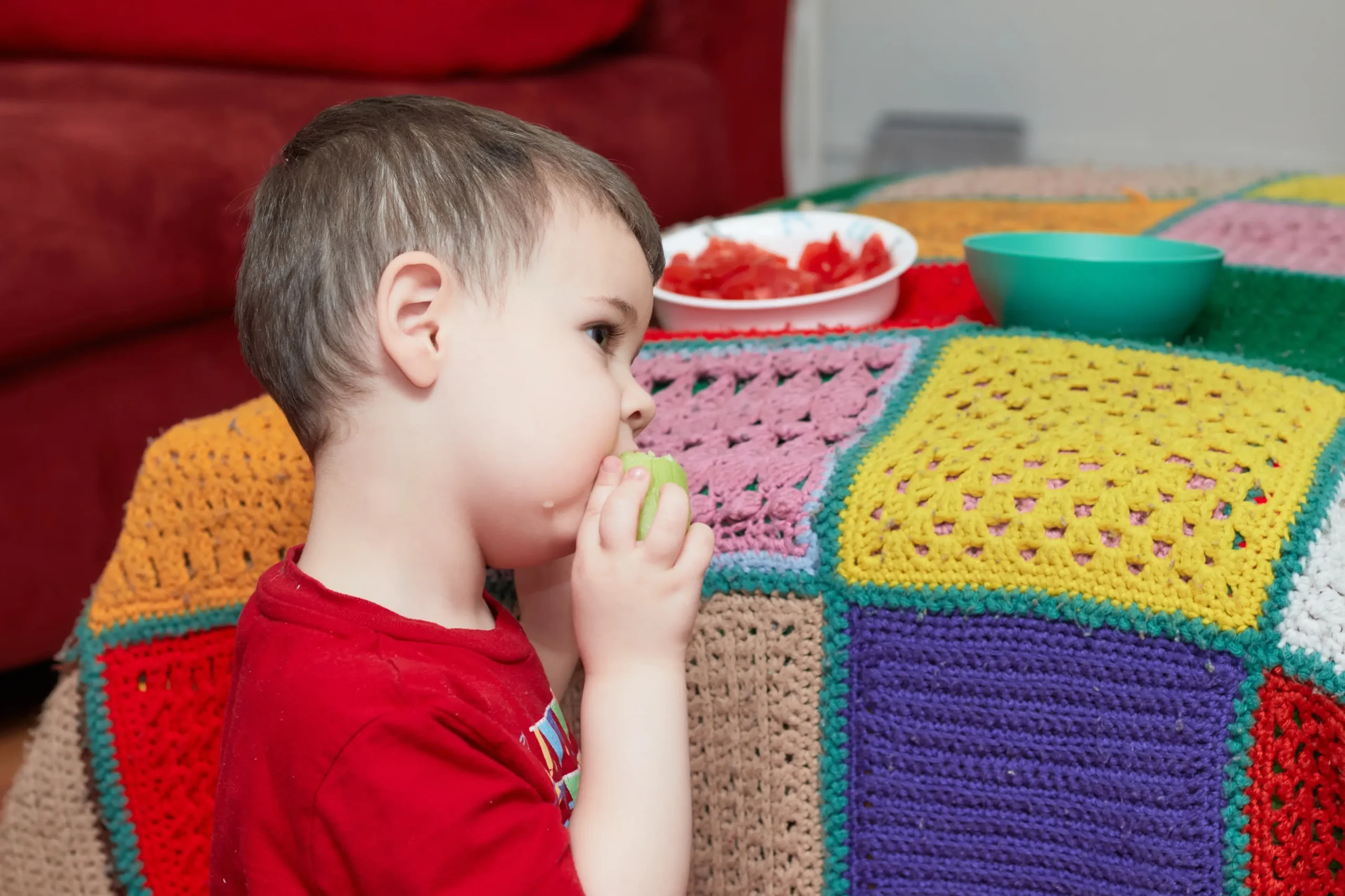 Chlapeček jí a sedí vedle gauče.