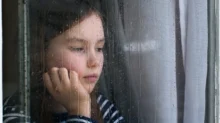 Holčička se smutně dívá z okna.
