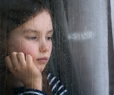 Holčička se smutně dívá z okna.