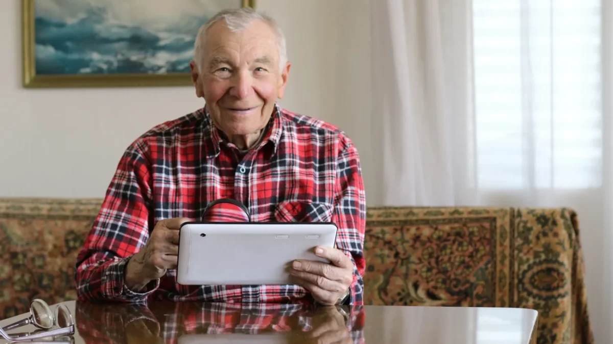 Děda s telefonem v ruce sedí u stolu.