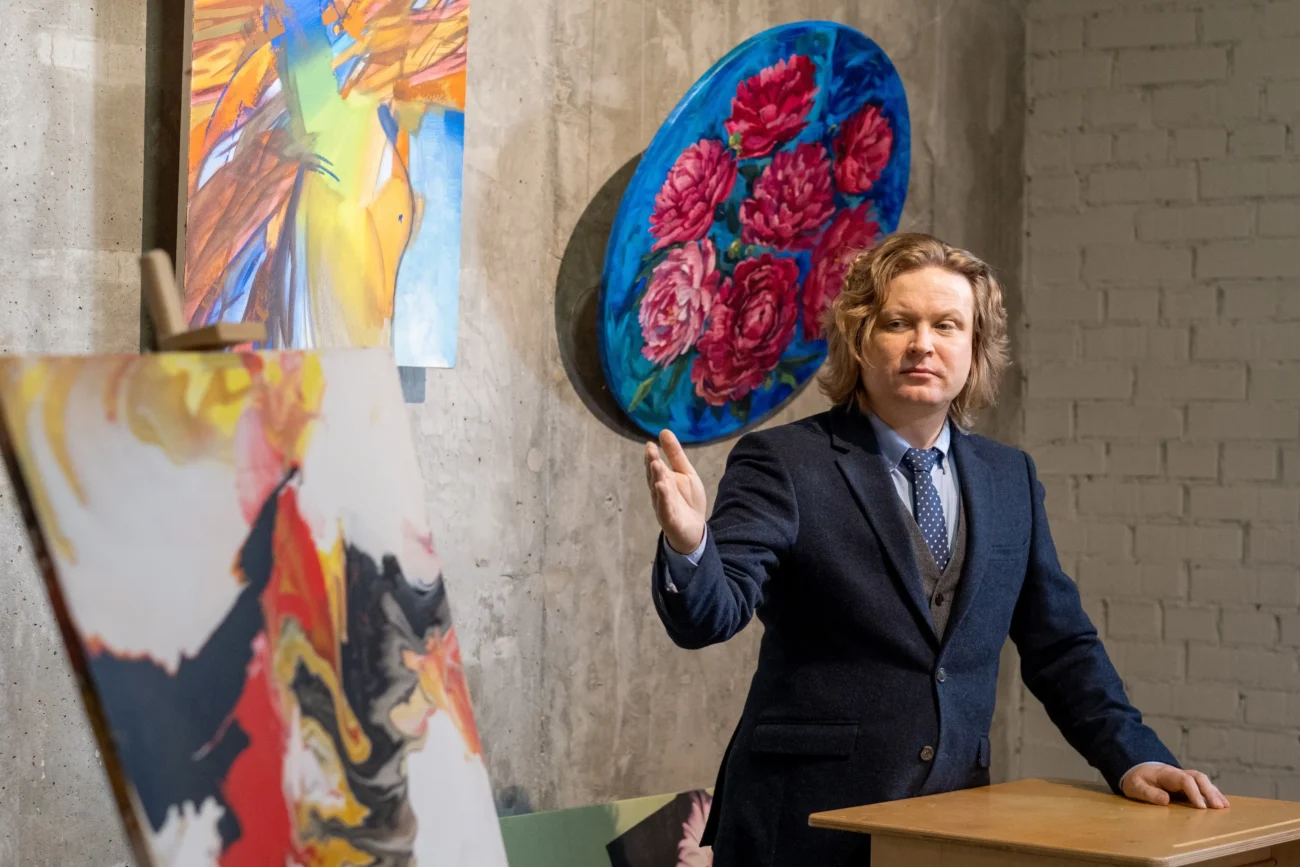 Muž stojí před obrazy na aukci. 