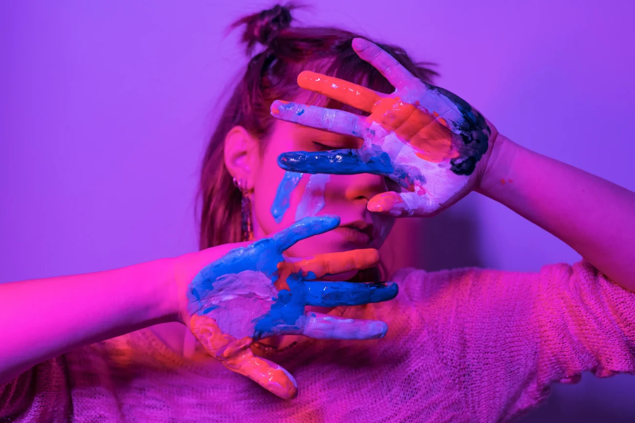 Žena si pomalovanýma rukama skrývá obličej. 