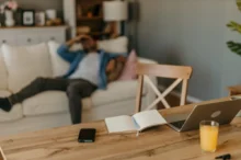 Na stole leží notebook s knihou a pitím.