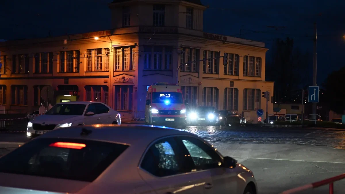 Před domem stojí auta a sanitka.