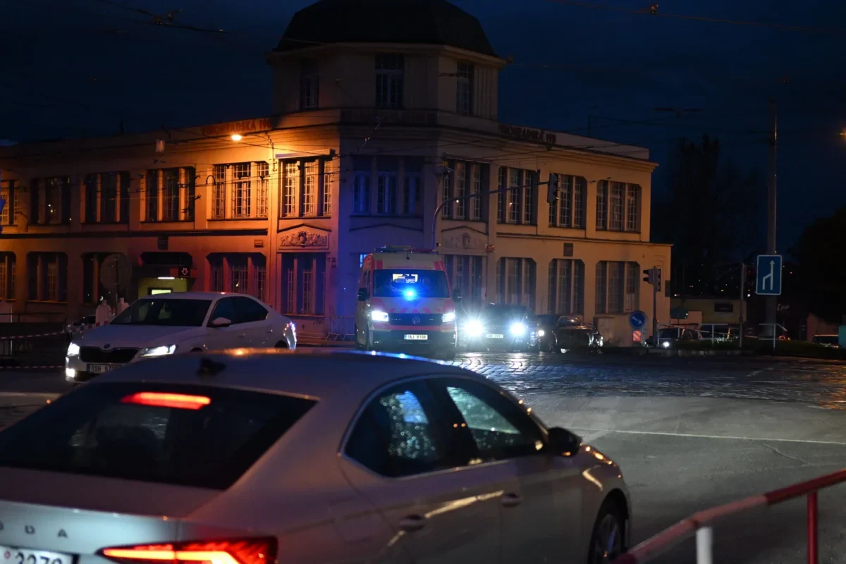 Před domem stojí auta a sanitka.