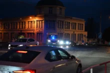 Před domem stojí auta a sanitka.