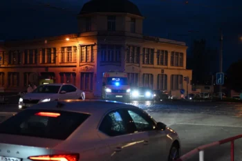 Před domem stojí auta a sanitka.