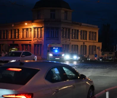 Před domem stojí auta a sanitka.