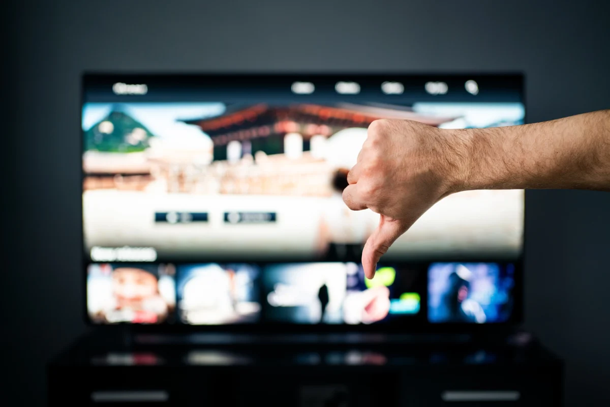 Mužská ruka ukazující palec dolů před televizní obrazovkou
