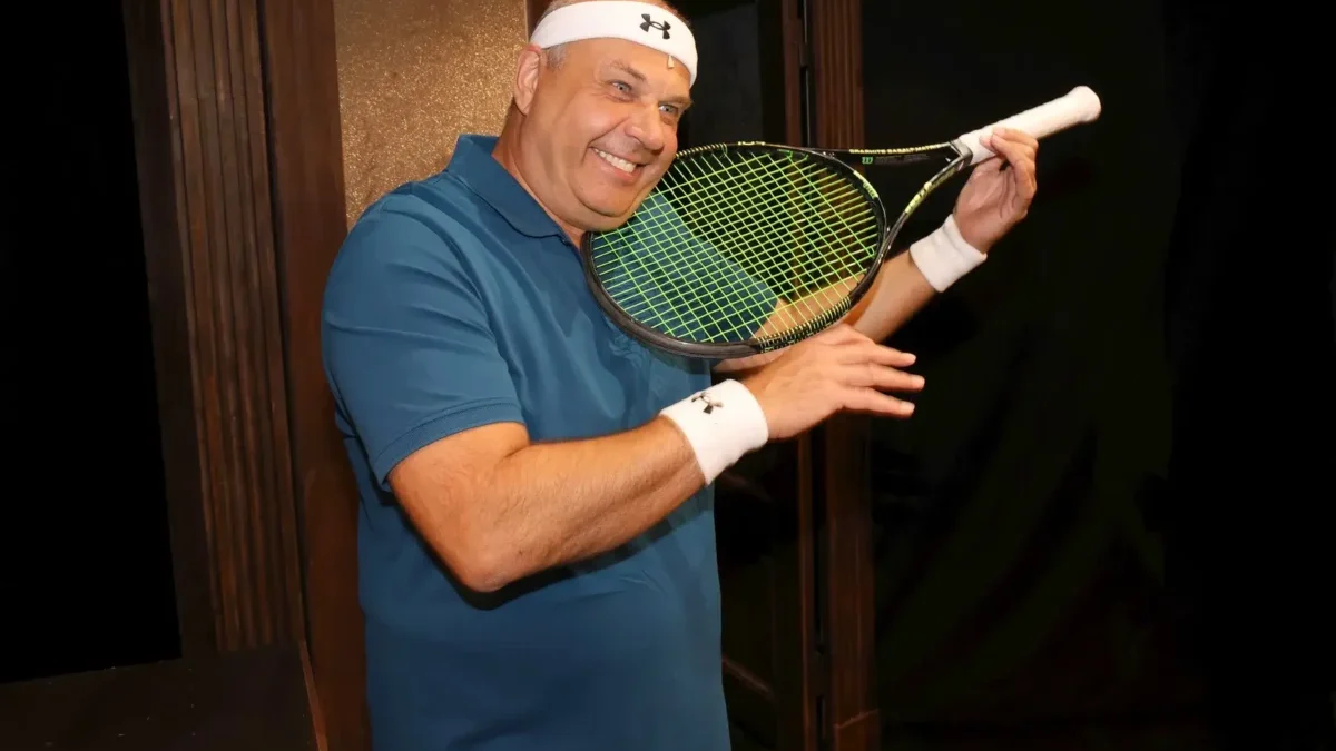 Petr Rychlý má v ruce tenisovou raketu a usmívá se.