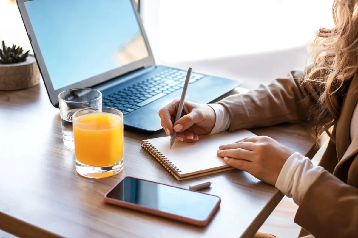 Žena sedí u notebooku a něco si píše do notýsku.