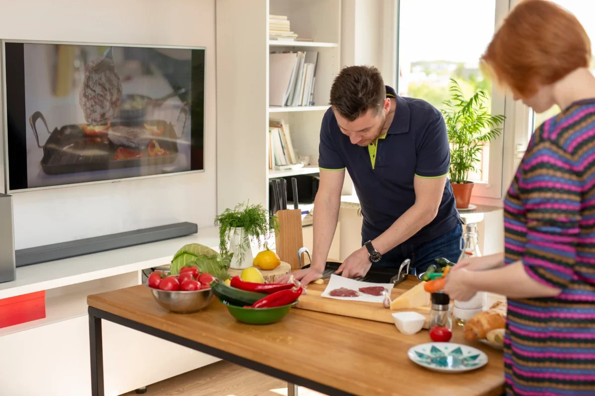 Lidé připravující jídlo v kuchyni u televize.