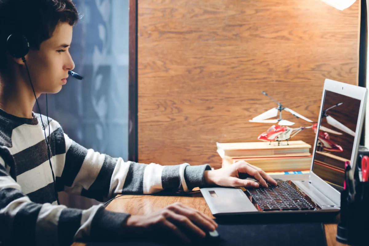 Chlapec sedí u notebooku a má sluchátka.