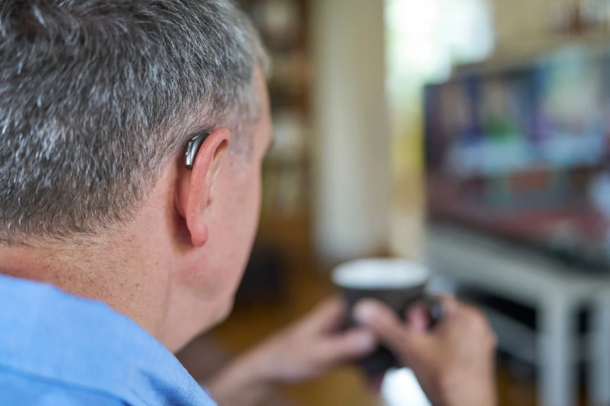 Muž s naslouchátkem sedí u TV.