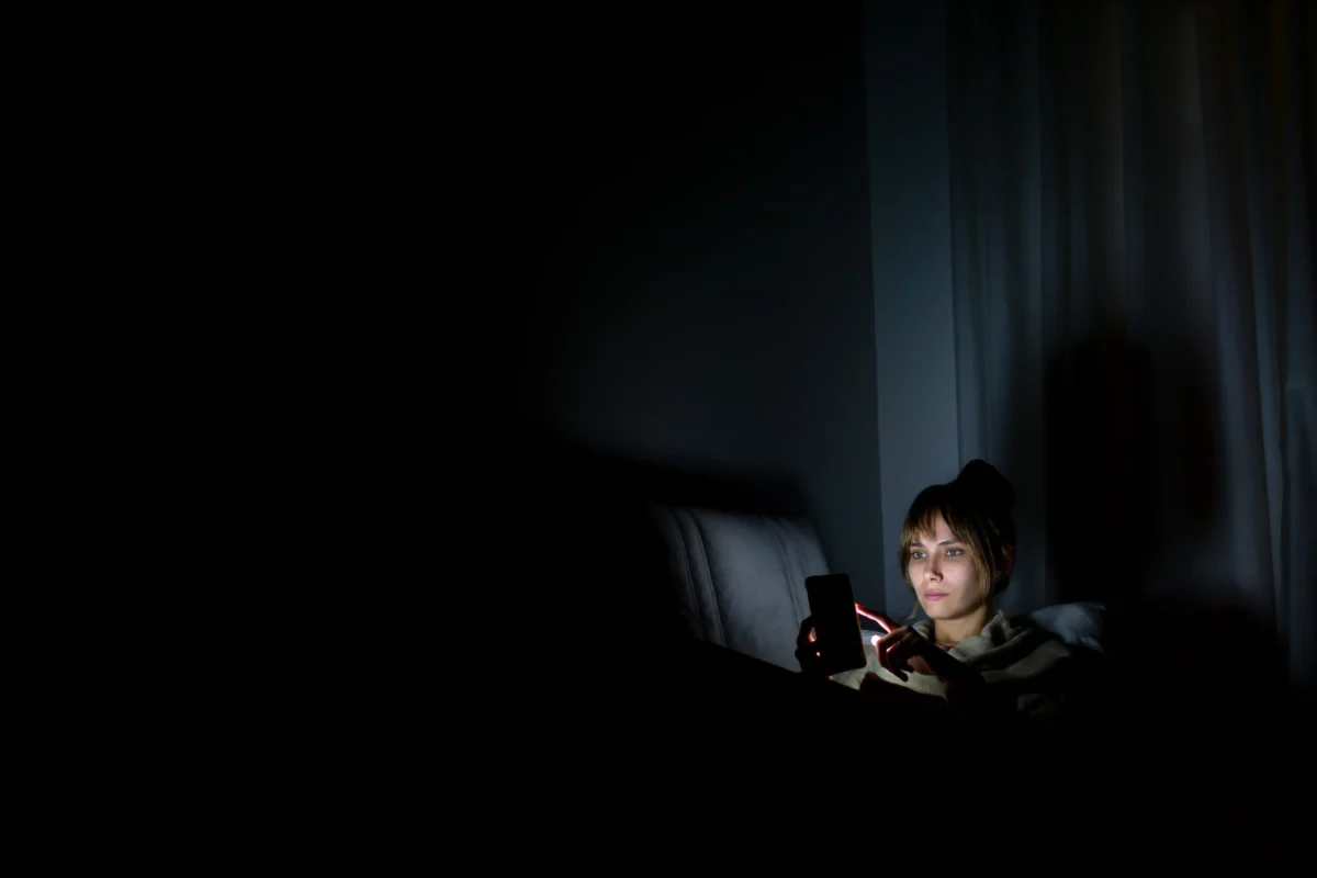 Žena se v noci dívá do telefonu. 