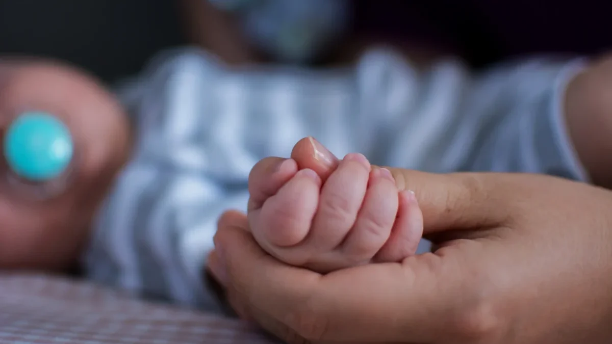 Člověk drží miminko za ruku.