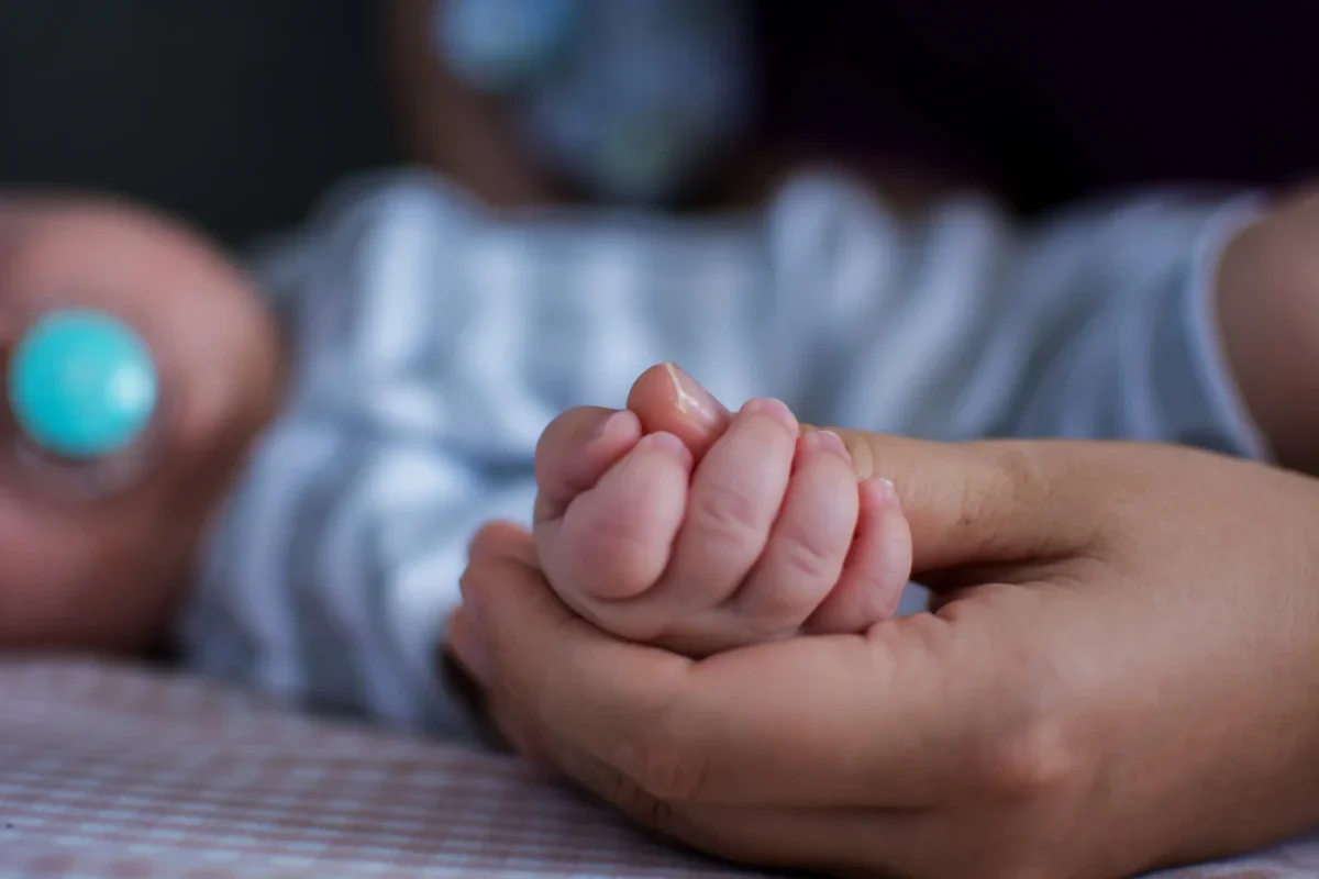 Člověk drží miminko za ruku.