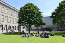 Studenti sedí na trávníku před školou.