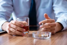 Člověk v jedné ruce drží cigaretu a v druhé sklenici s alkoholem.