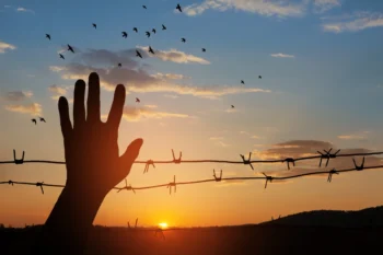 Ruka mává před ostnatým drátem.