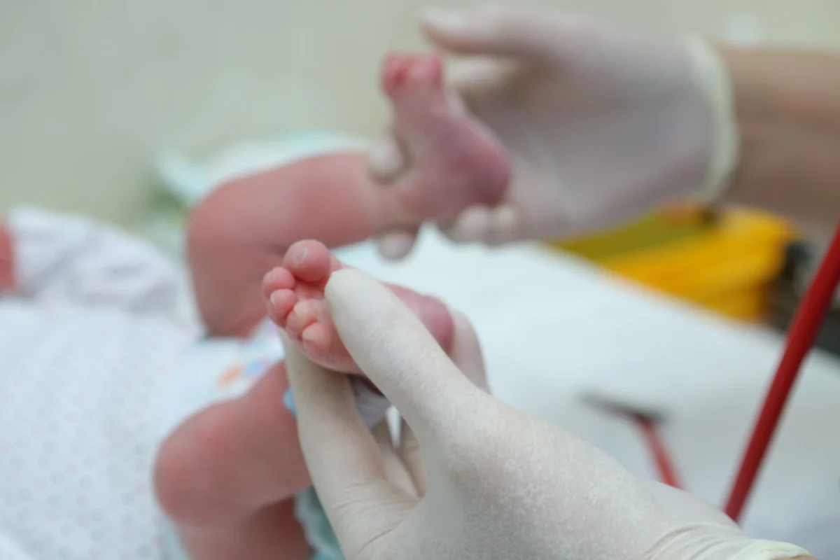 Sestřička drží v porodnici nohy miminka. 