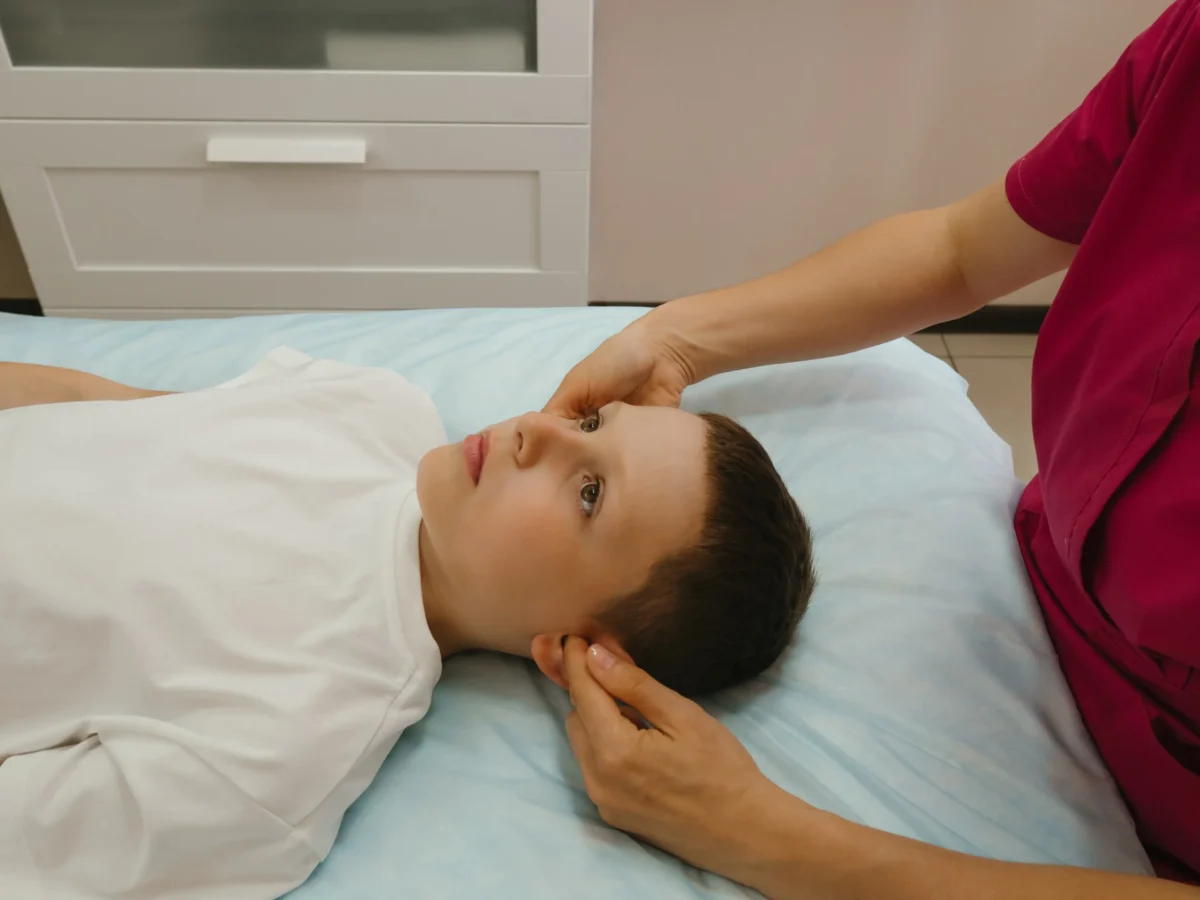 Chlapeček leží na zádech a někdo mu sahá na uši. 