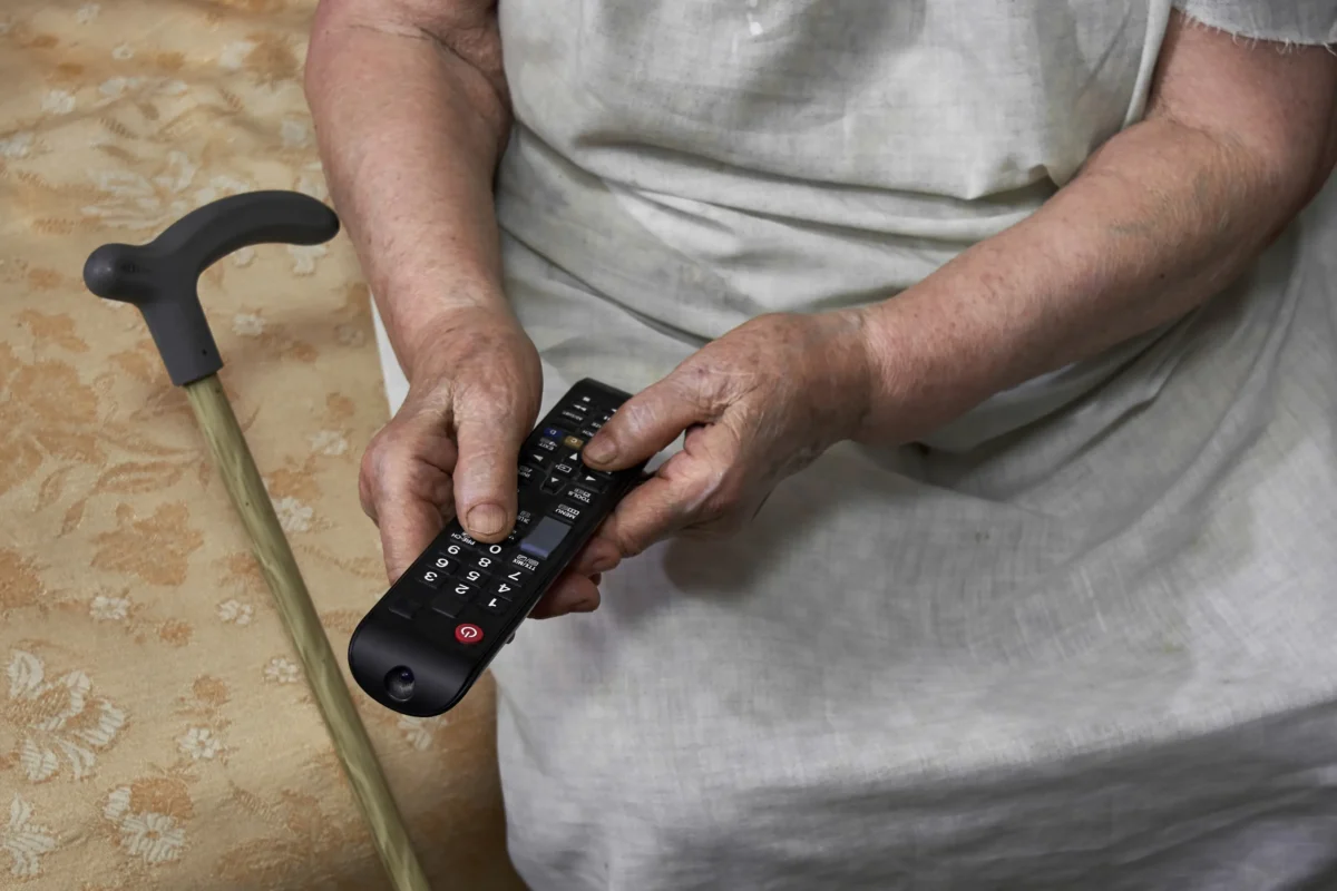 Starší žena v ruce drží ovladač od TV.