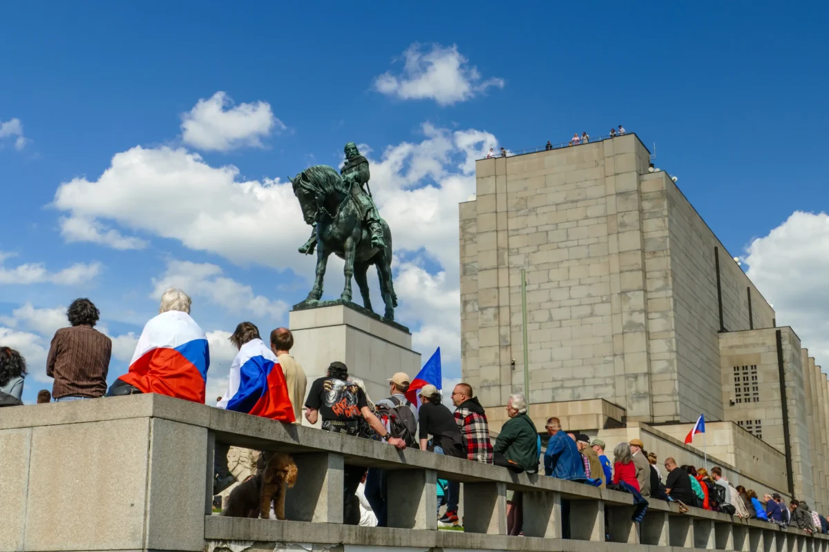 Lidé stojí s vlajkami kolem sochy.