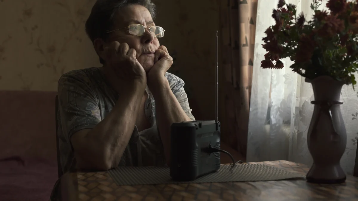 Babička sedí u stolu s rádiem. 