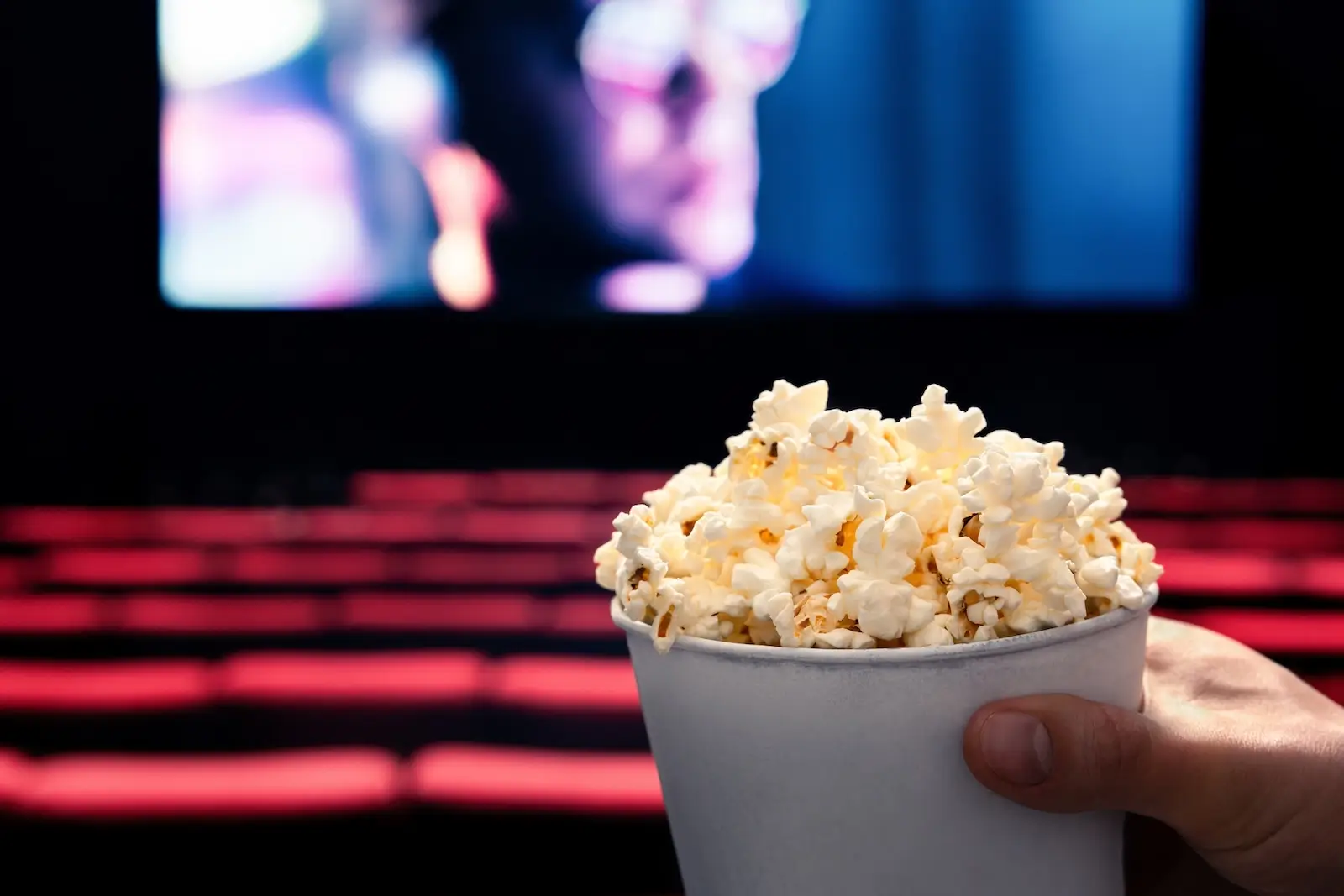 Popcorn zvedá tržby kin. Zdroj: Shutterstock | TVGURU.cz Člověk v kině v ruce drží popcorn.