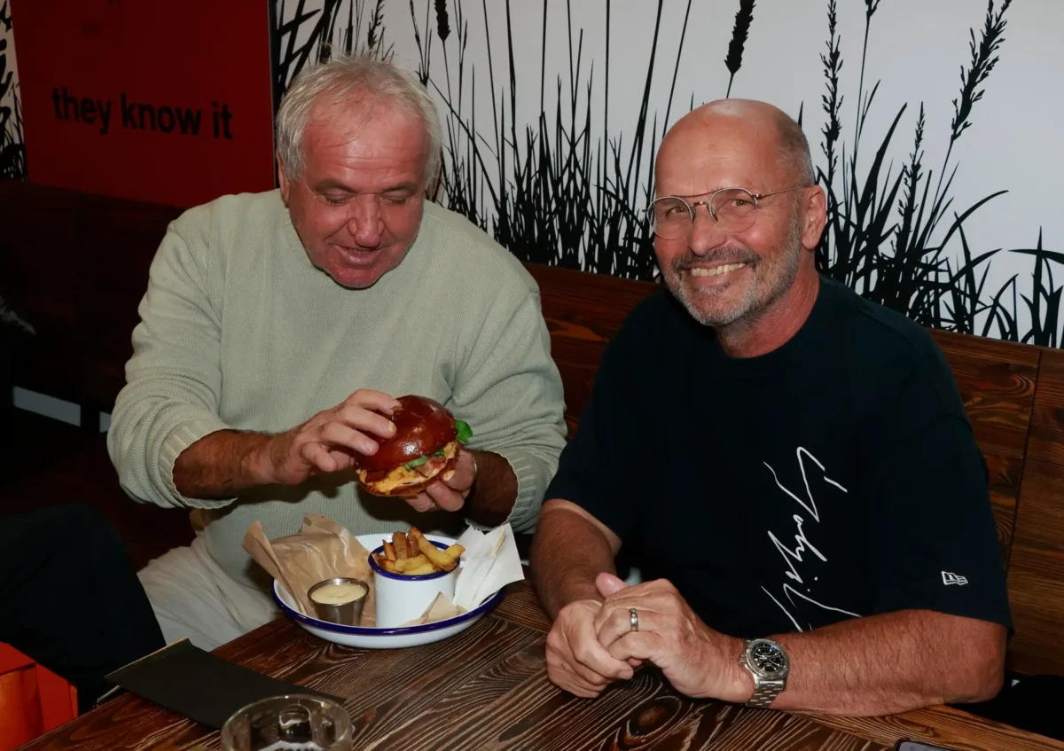 Kuchař Zdeněk Pohlreich sedí vedle pána s hamburgerem. 