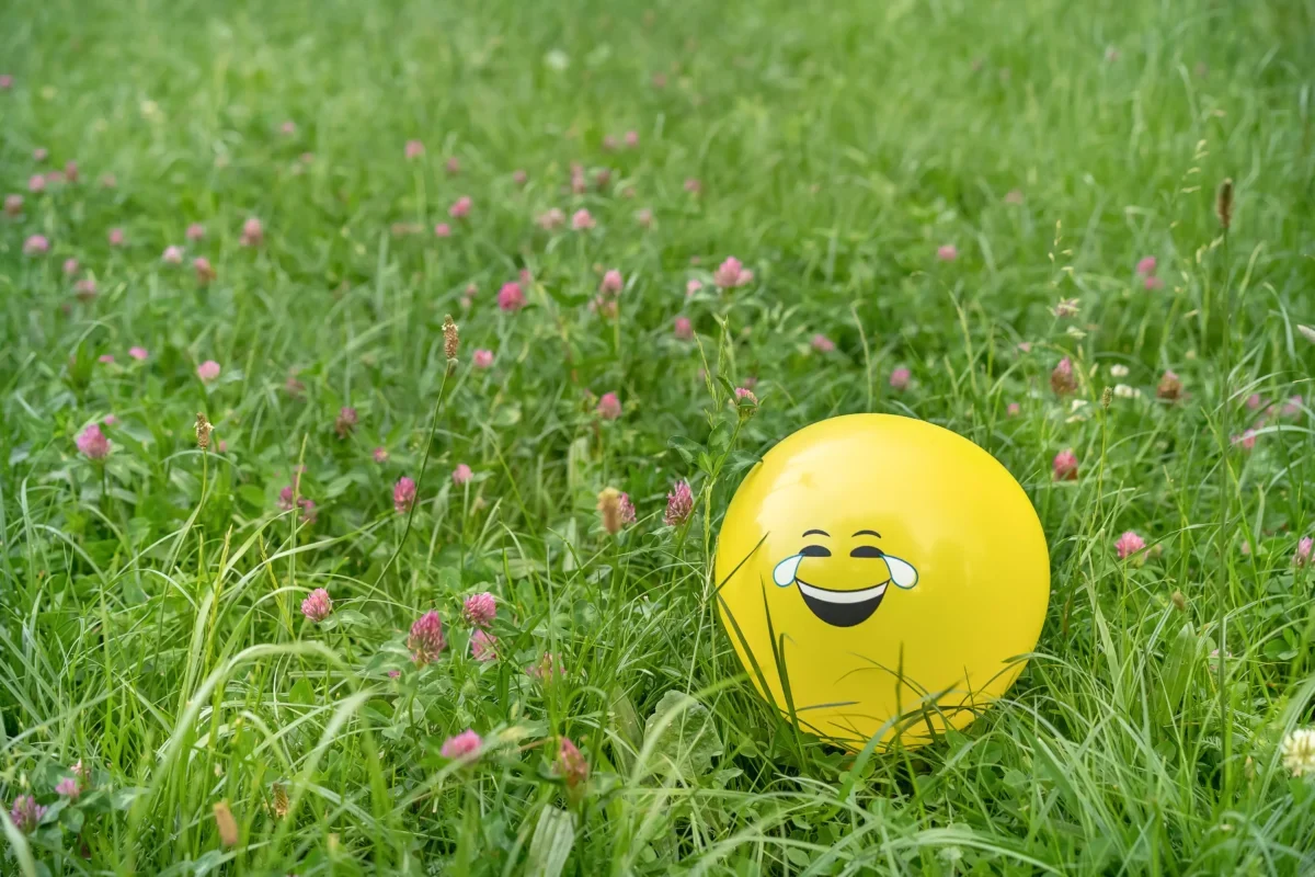 V trávě se válí balonek s nakresleným úsměvem.