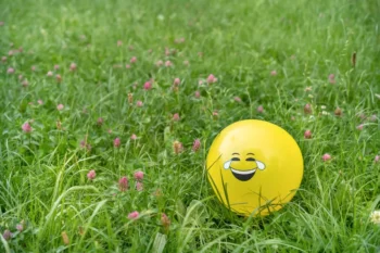 V trávě se válí balonek s nakresleným úsměvem.