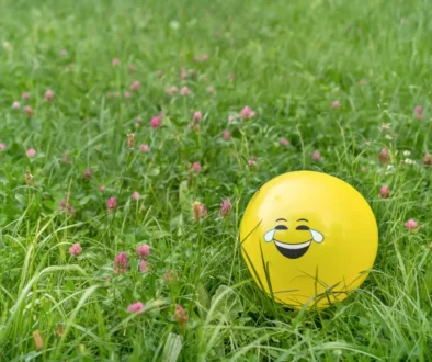 V trávě se válí balonek s nakresleným úsměvem.