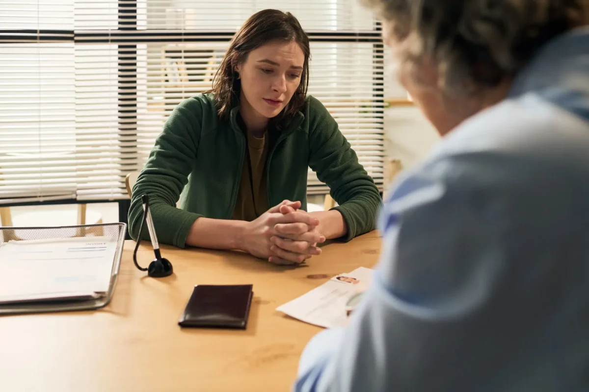 Žena sedí za stolem a tváří se smutně. 