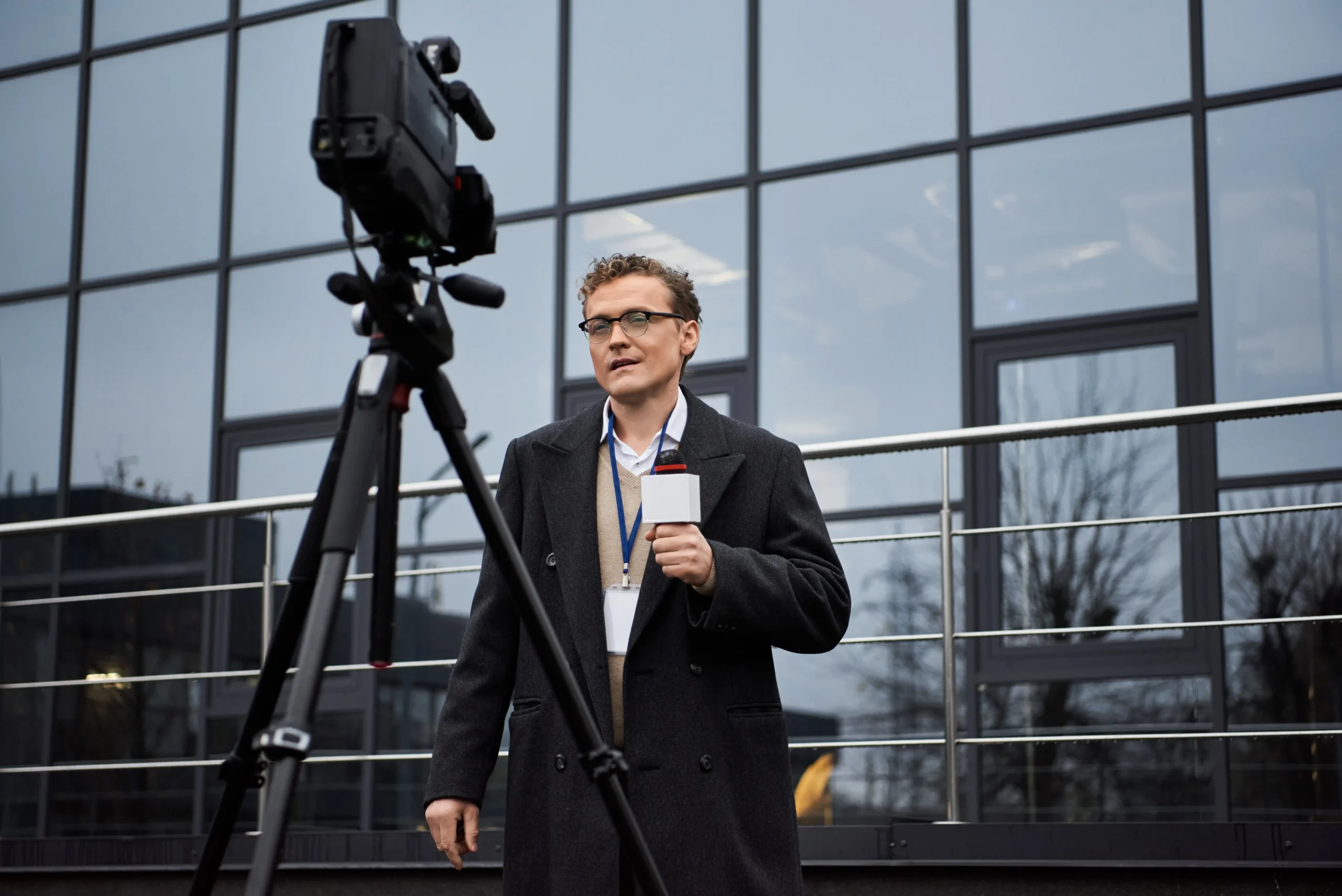 Muž stojí před televizní kamerou s mikrofonem v ruce.