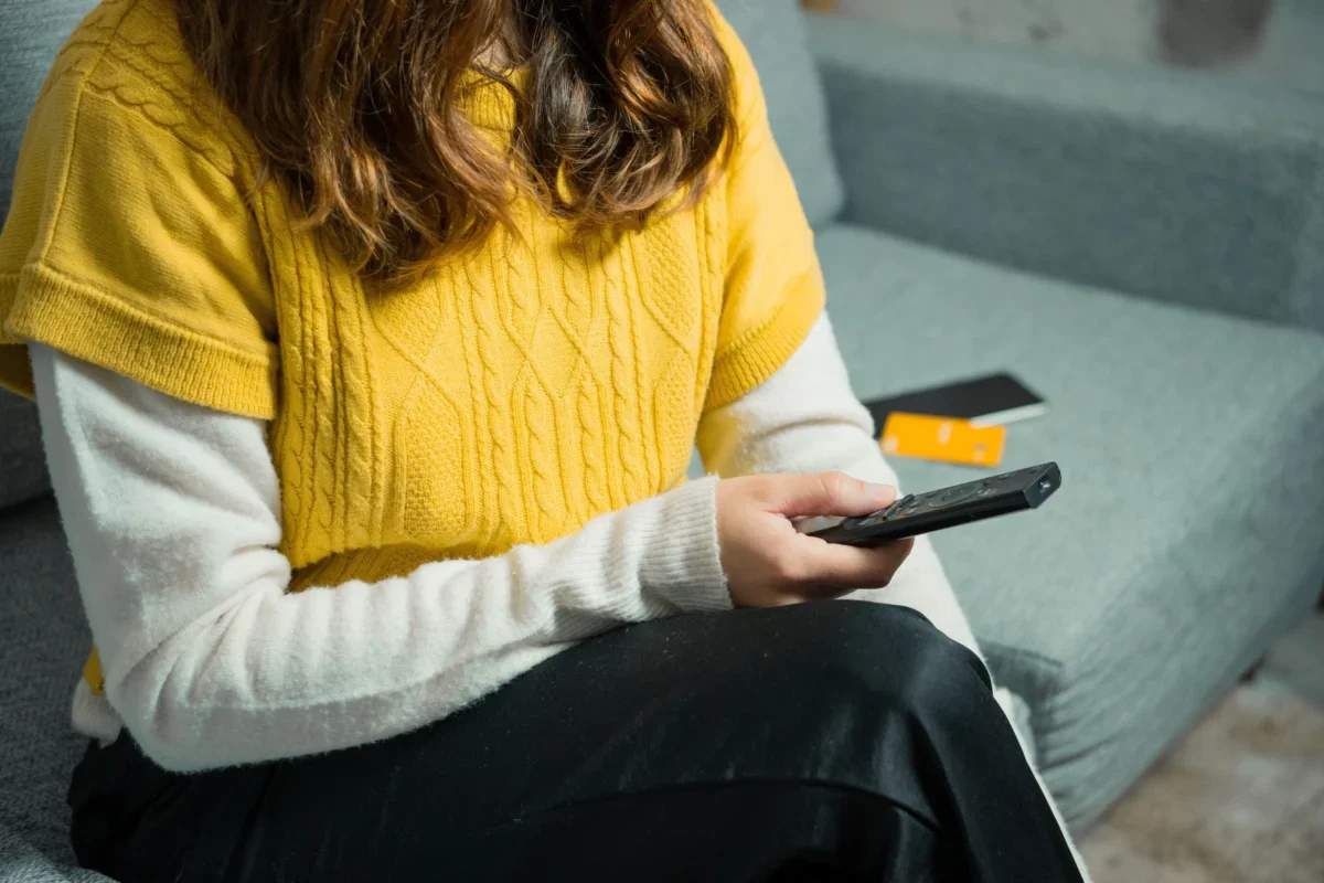 Žena sedí na gauči a v ruce drží ovladač.