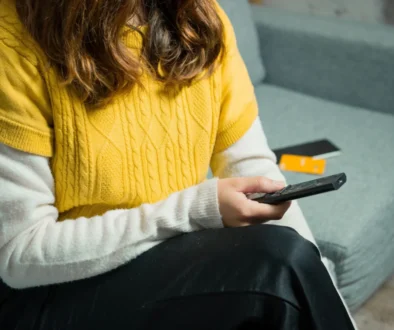 Žena sedí na gauči a v ruce drží ovladač.